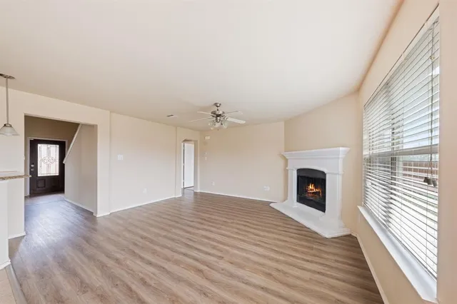 a view of an empty room with wooden floor fireplace and a window