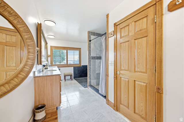 169 Taylor Road, Unit 101 Grantsville, UT 84029 - Photo 20 of 47 Main home - Expansive master Bathroom featuring a wood-panel door with decorative fluted trim, a double vanity with stone countertops and undermount sinks, a large mirror with an ornate carved wood frame, a window with wood plantation shutters, and a tile