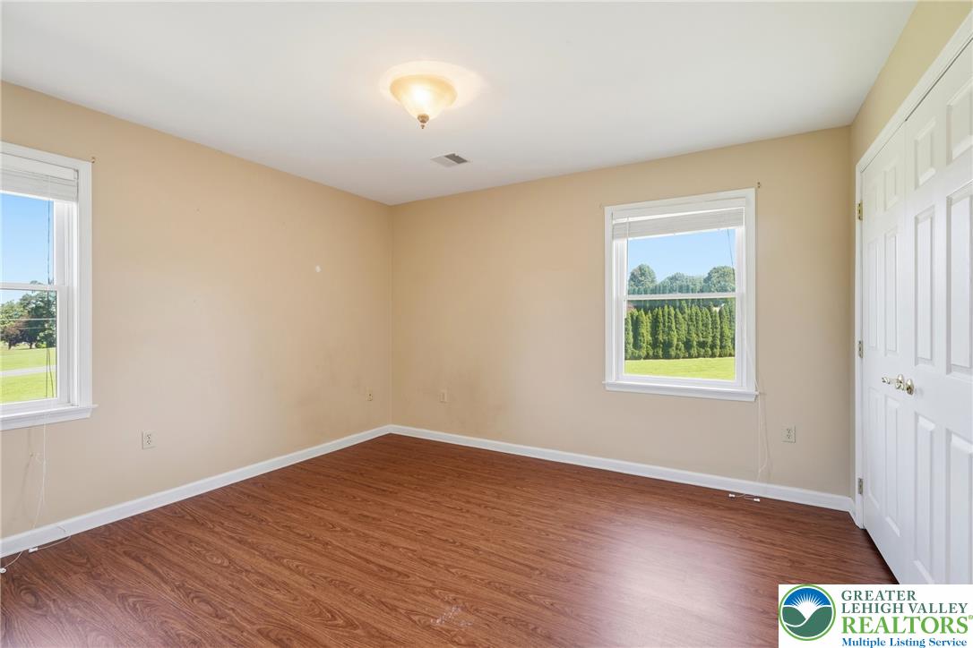 590 Fehr Road Nazareth, PA 18064 - Photo 39 of 79 Gleaming wood-inspired floors anchor a sunlit bedroom framed by dual windows showcasing green lawn views.