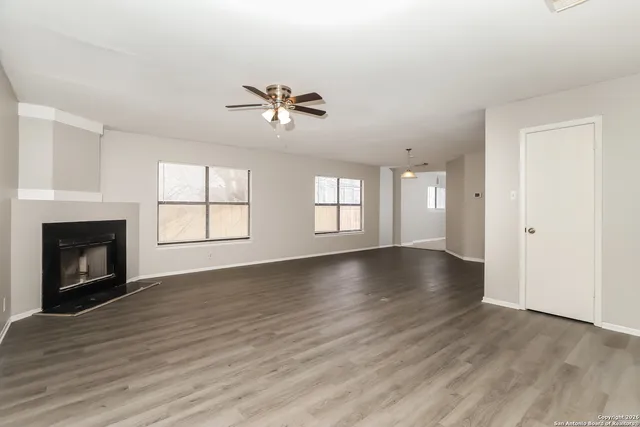 an empty room with wooden floor fireplace and windows