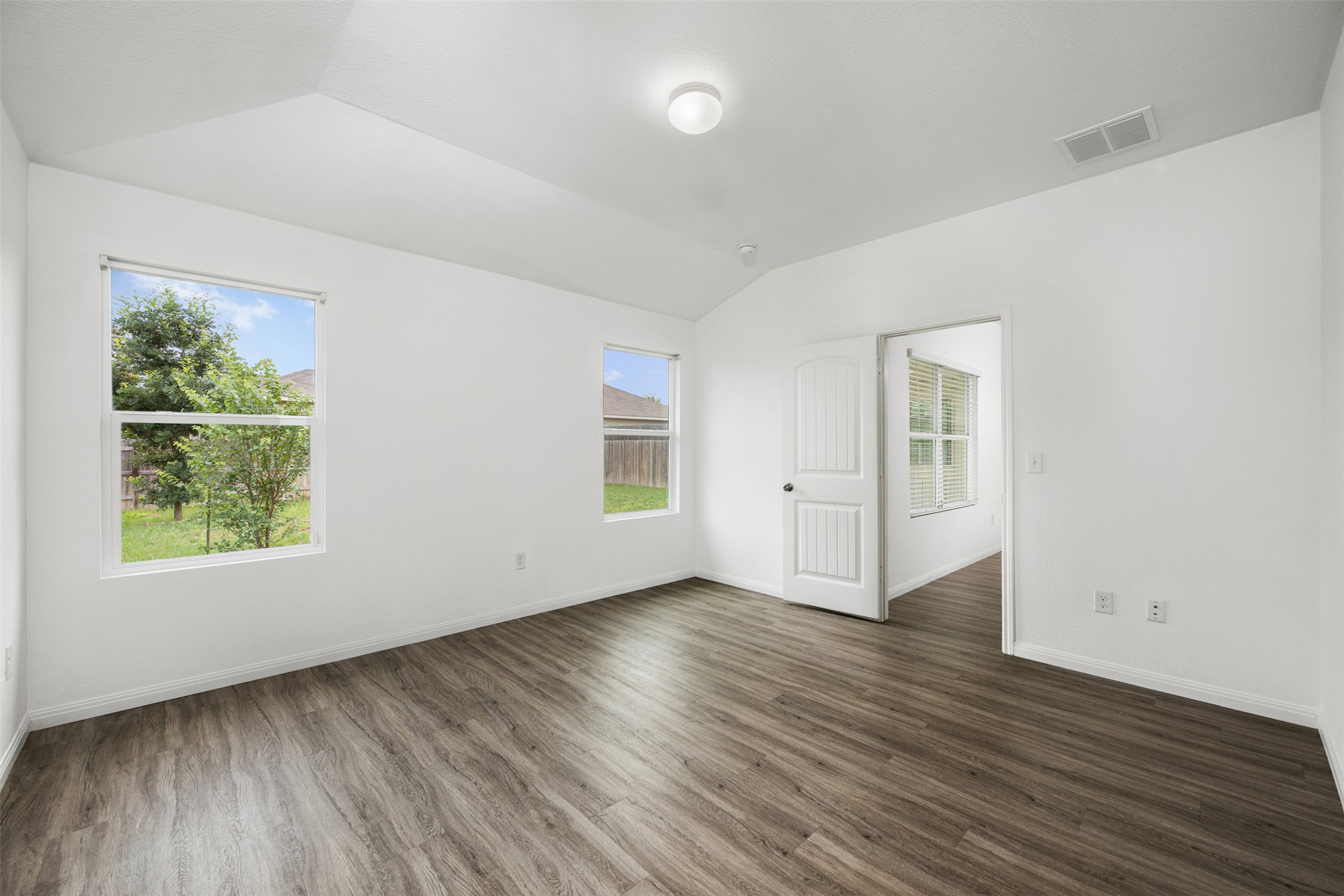 14900 Retha Pass Austin, TX 78725 - Photo 15 of 39 Spacious room featuring vaulted ceilings, wood-finish flooring, two large windows, a white paneled door, and neutral white walls