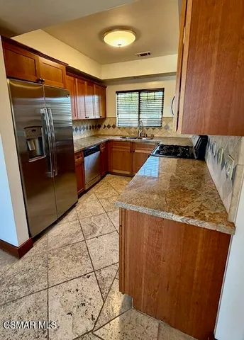 a kitchen with stainless steel appliances granite countertop a refrigerator a stove and a sink with wooden cabinets