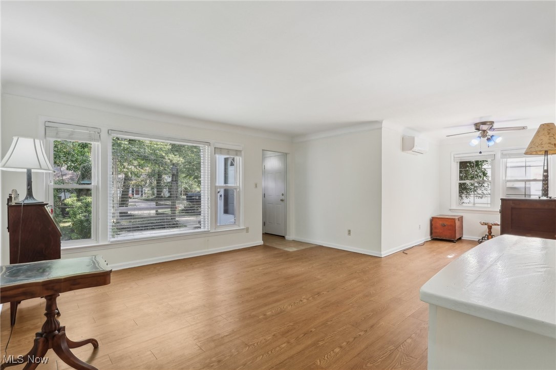 Living room with a wall mounted AC, light wood-type flooring, ceiling fan, and crown molding