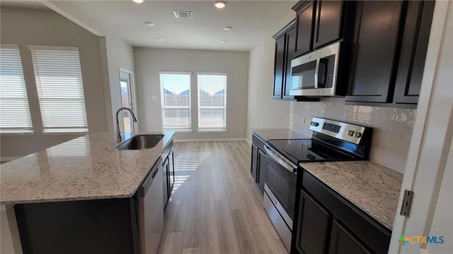 a kitchen with granite countertop stainless steel appliances a sink stove top oven and cabinets