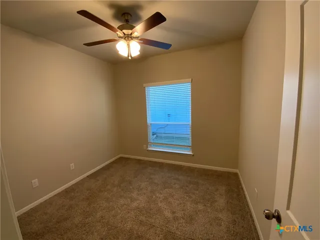 an empty room with a chandelier fan and windows
