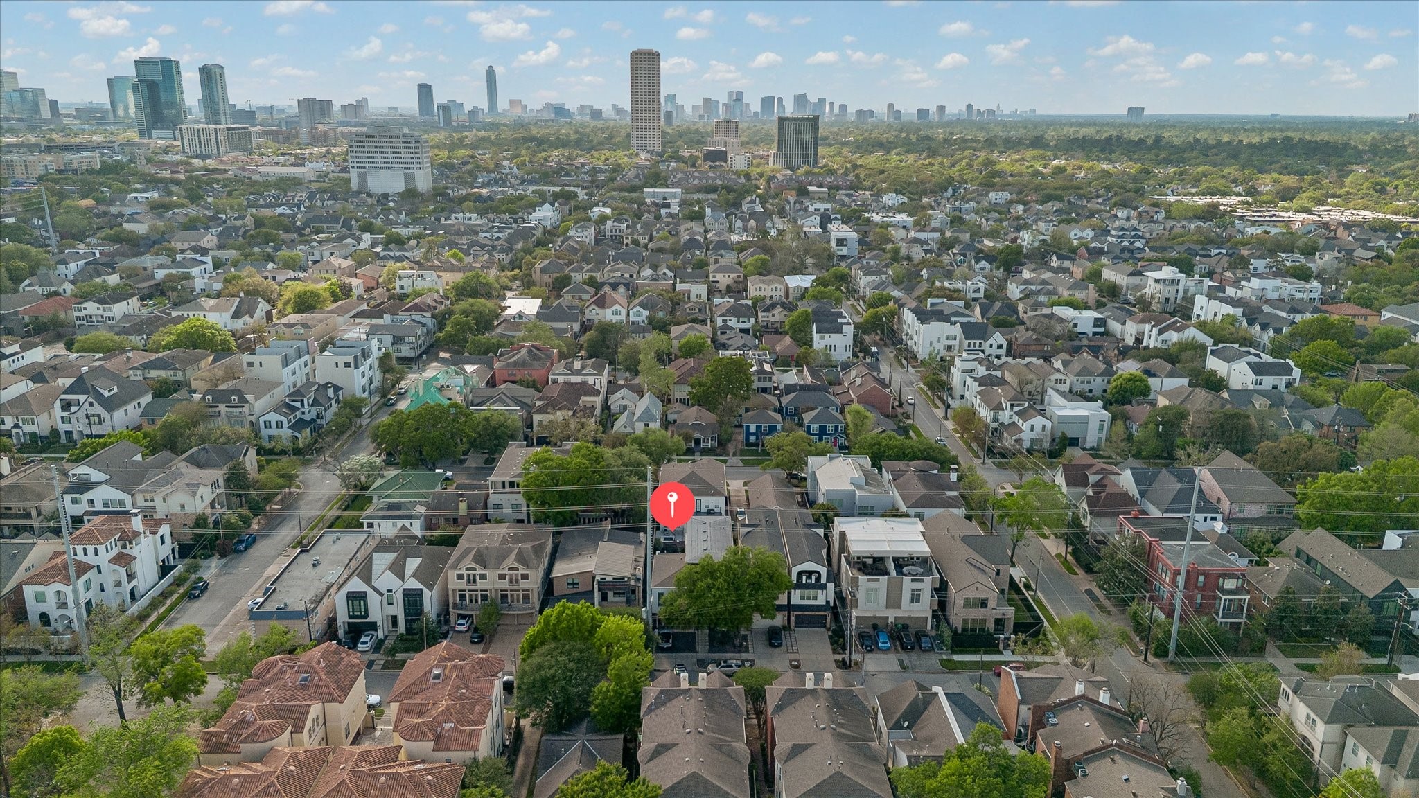 2014 Park Street Houston, TX 77019 - Photo 40 of 40 This aerial photo showcases a suburban neighborhood with a mix of modern and traditional homes, surrounded by lush greenery. The area appears well-developed, with a city skyline visible in the distance, indicating proximity to urban amenities.