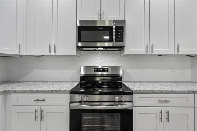 a kitchen with stainless steel appliances granite countertop white cabinets and a stove top oven