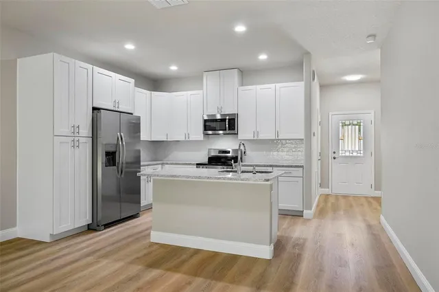 a kitchen with stainless steel appliances granite countertop a stove a refrigerator a sink and white cabinets with wooden floor
