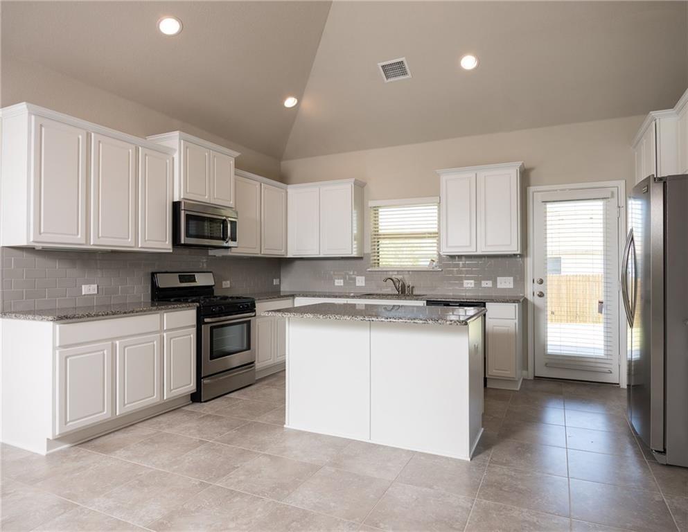 641 Schefer Street Leander, TX 78641 - Photo 5 of 17 Spacious kitchen featuring white cabinetry, gray subway tile backsplash, stainless steel appliances, a center island with countertop, and neutral tile flooring