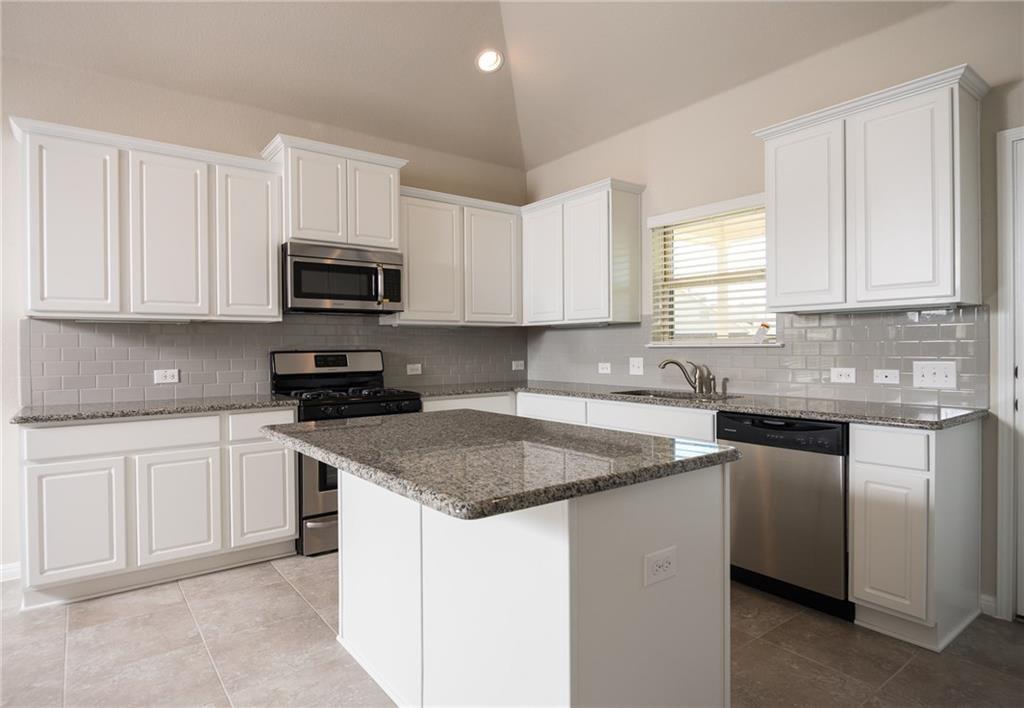 641 Schefer Street Leander, TX 78641 - Photo 6 of 17 Bright kitchen featuring white cabinetry, granite countertops, a central island, stainless steel appliances, and a subway tile backsplash