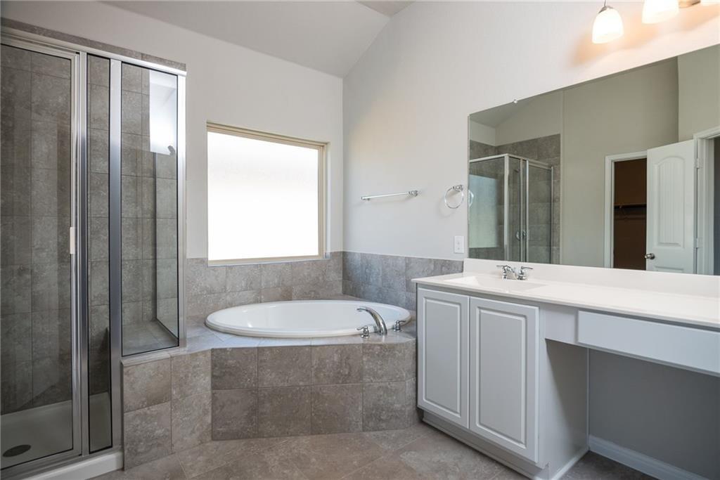 641 Schefer Street Leander, TX 78641 - Photo 8 of 17 Spacious bathroom featuring a built-in soaking tub, a separate glass-enclosed shower, a double vanity with a full-width mirror, and a frosted window