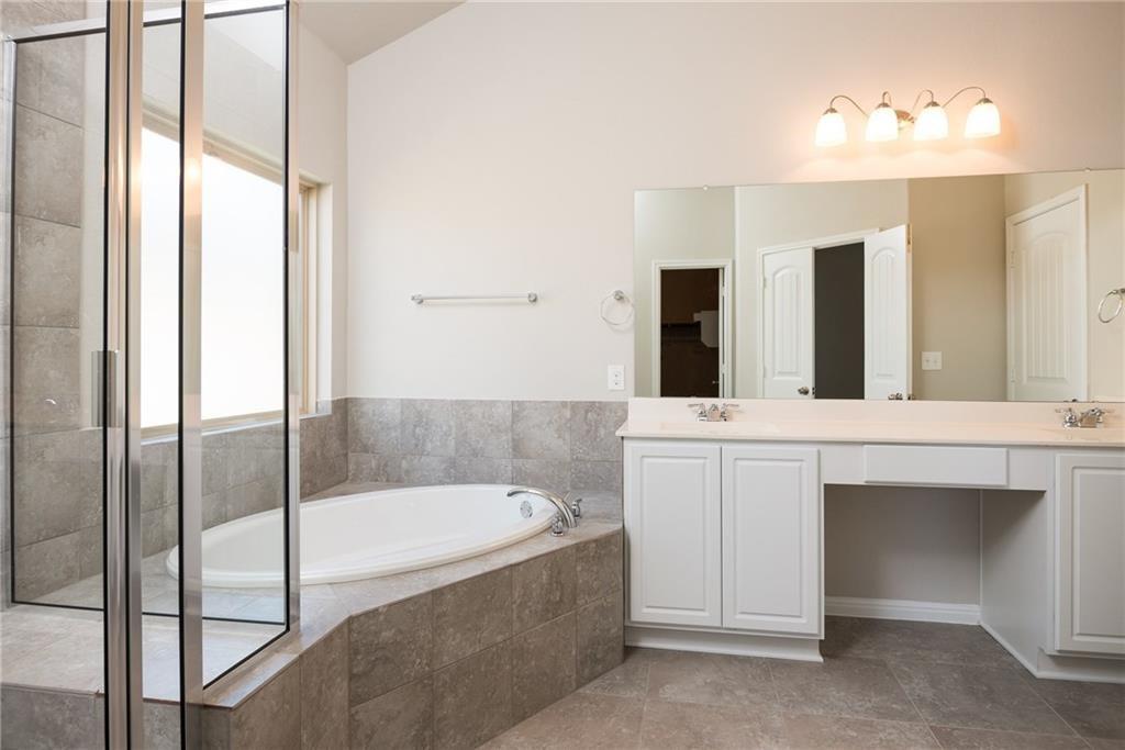 641 Schefer Street Leander, TX 78641 - Photo 9 of 17 Bathroom featuring a built-in soaking tub, glass-enclosed shower, dual vanities with white cabinetry, and a full-width mirror