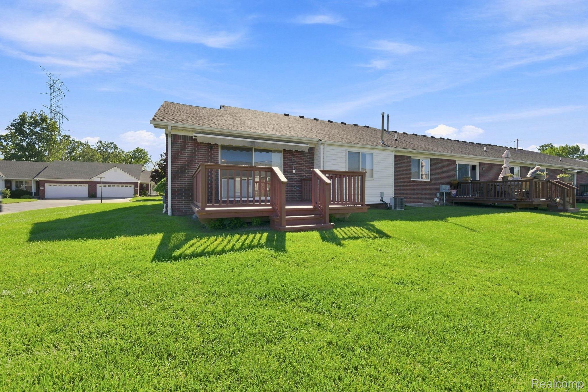 493 Harvard Drive Romeo, MI 48065 - Photo 30 of 36 Brick exterior with a wood-finish deck, sliding glass door access, and a large grassy yard
