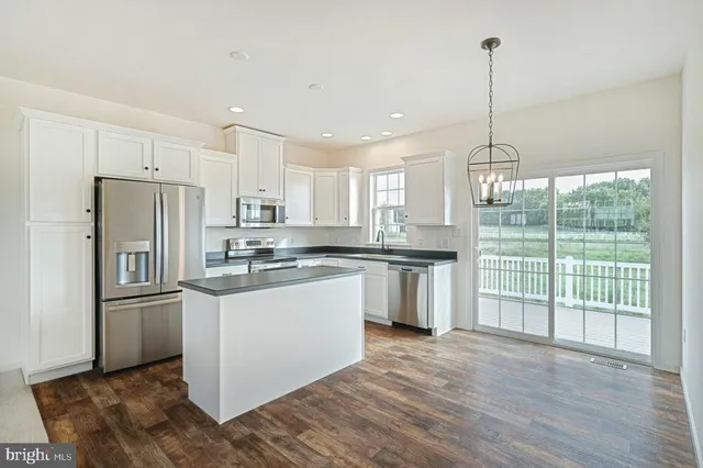 a kitchen with stainless steel appliances granite countertop a refrigerator a sink dishwasher a stove and white cabinets with wooden floor