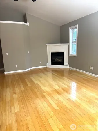 an empty room with wooden floor fireplace and windows