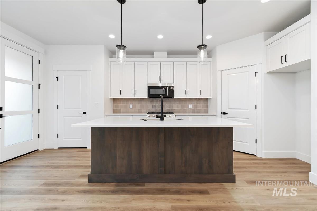 736 South Calhoun Lane Star, ID 83669 - Photo 10 of 42 Kitchen with two tone cabinets, a center island with sink, hanging light fixtures, light wood finished floors, and tasteful backsplash
