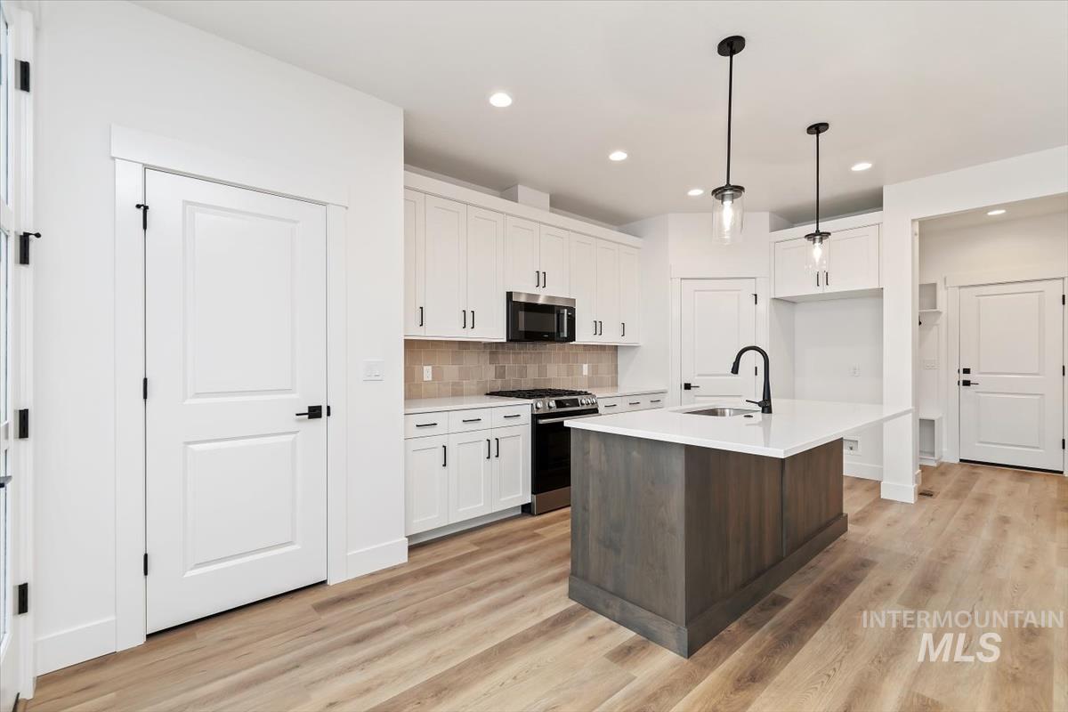 736 South Calhoun Lane Star, ID 83669 - Photo 6 of 42 Two tone kitchen with two tone cabinets, a kitchen island with sink, stainless steel appliances, decorative light fixtures, and light wood-style floors