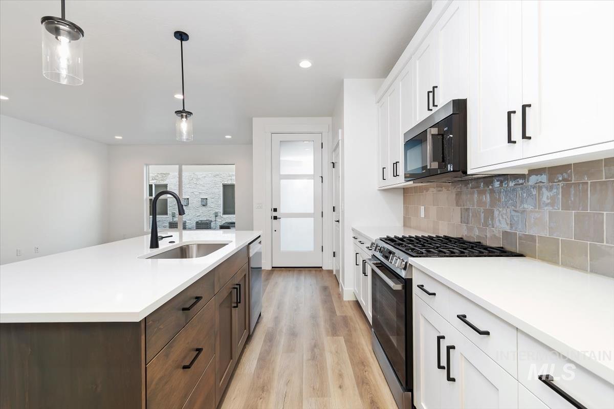 736 South Calhoun Lane Star, ID 83669 - Photo 7 of 42 Two tone kitchen with two tone cabinets, stainless steel appliances, pendant lighting, light wood-type flooring, and tasteful backsplash