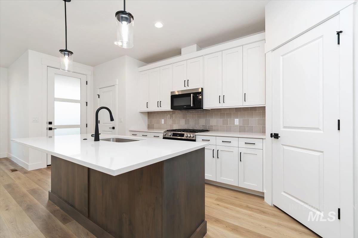 736 South Calhoun Lane Star, ID 83669 - Photo 8 of 42 Kitchen with light wood finished floors, two tone cabinetry, an island with sink, stainless steel appliances, and pendant lighting