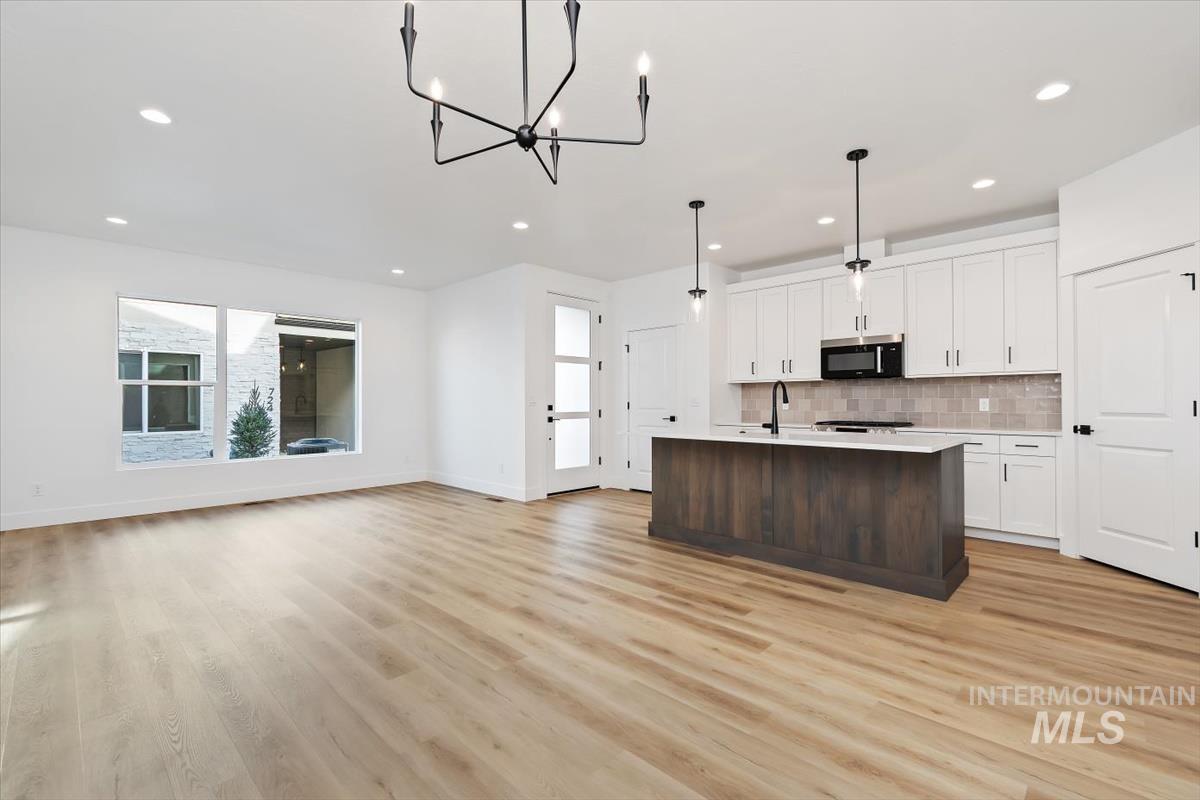 736 South Calhoun Lane Star, ID 83669 - Photo 41 of 42 Dual tone kitchen with open floor plan, a kitchen island with sink, two tone cabinetry, suspended lighting, and stainless steel microwave