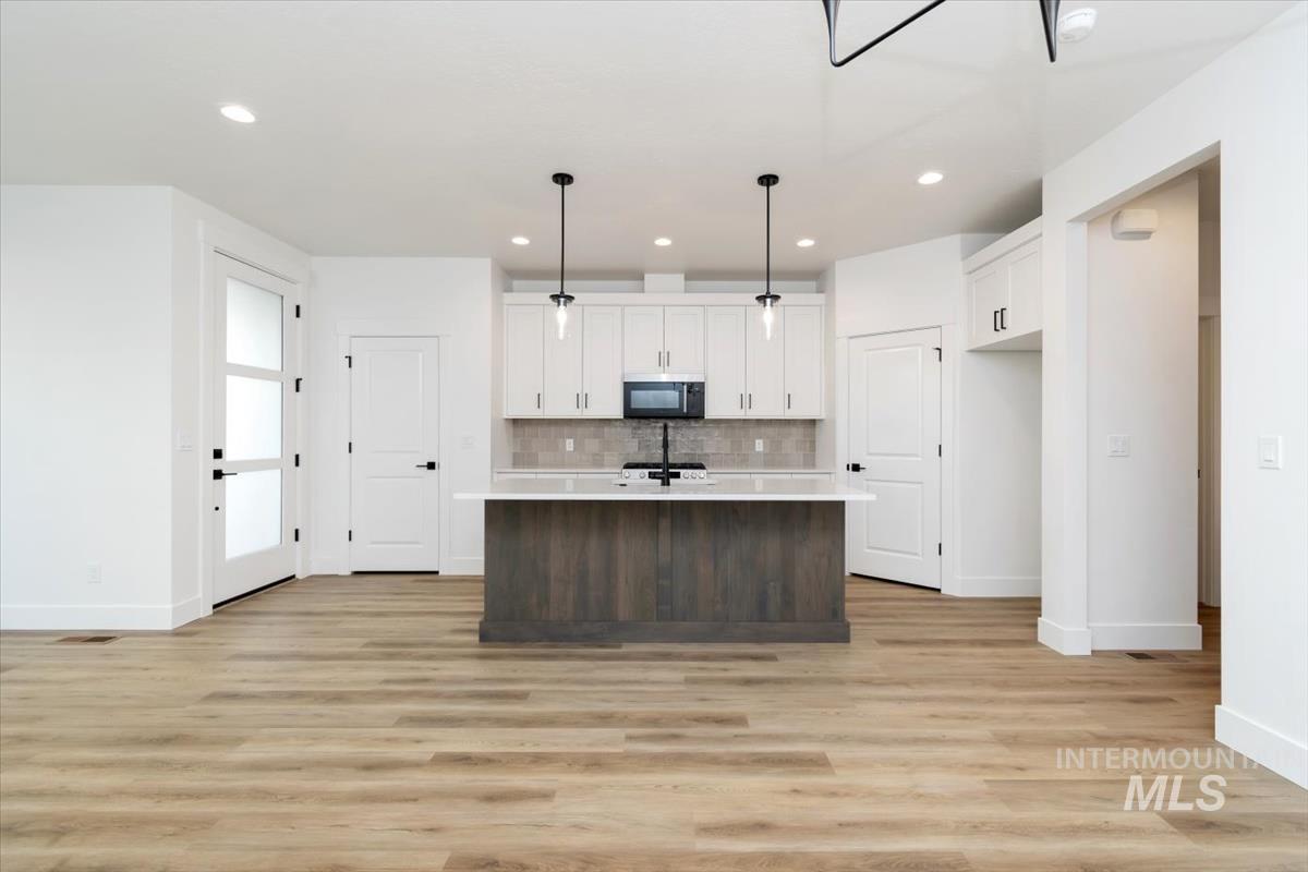 736 South Calhoun Lane Star, ID 83669 - Photo 9 of 42 Two tone kitchen with an island with sink, pendant lighting, light wood-type flooring, two tone color scheme, and black microwave