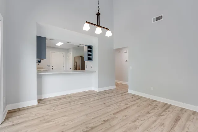 a view of an empty room and kitchen with wooden floor