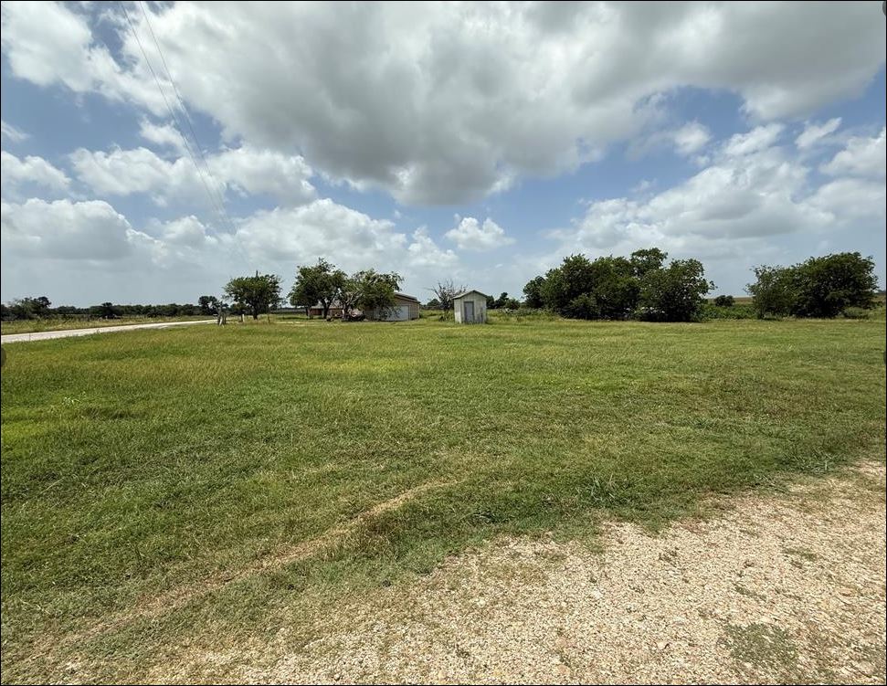Expansive grassy lot with scattered trees and a visible outbuilding