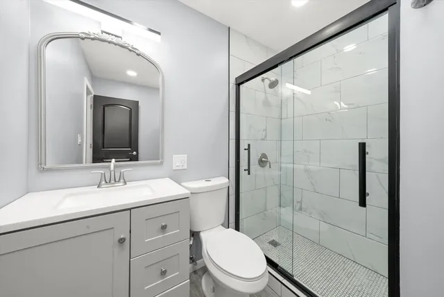 a bathroom with a toilet a sink a glass door a shower and a mirror