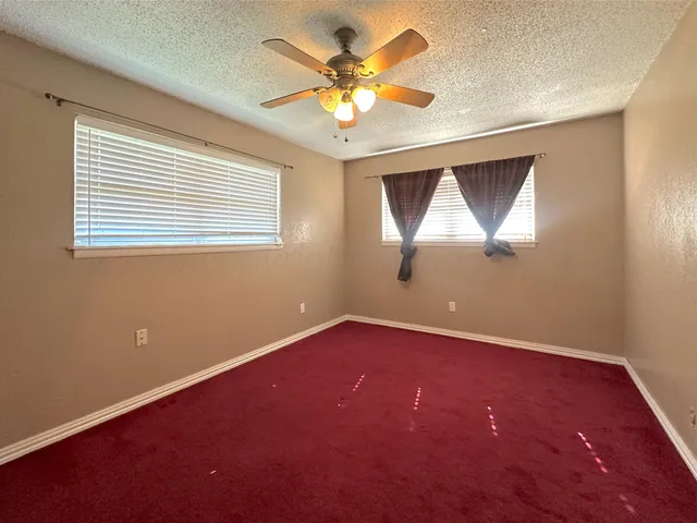 an empty room with a chandelier fan and windows