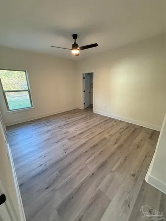 an empty room with wooden floor ceiling fan and windows