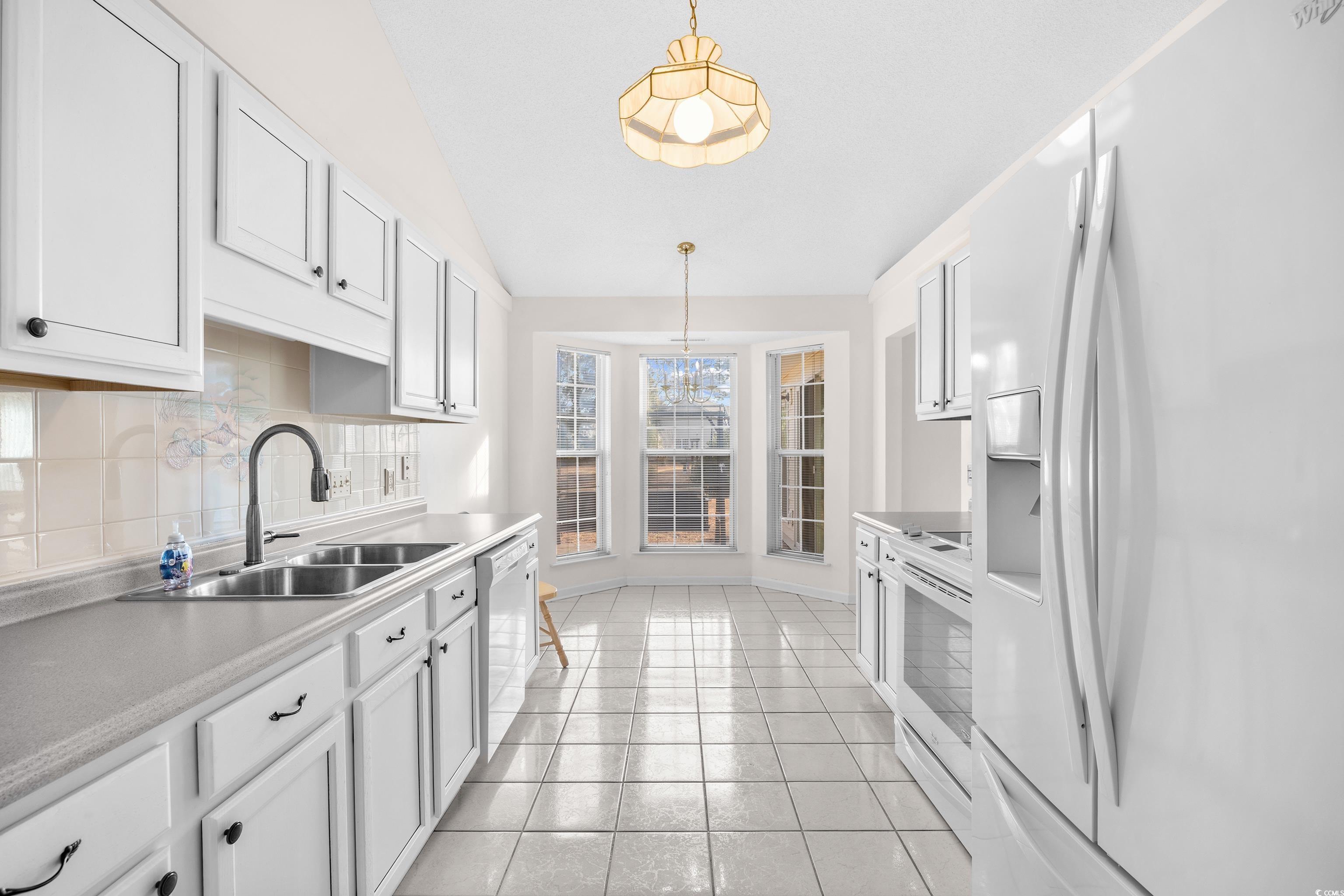 1744 Starbridge Drive Surfside Beach, SC 29575 - Photo 10 of 38 Kitchen with white appliances, backsplash, lofted ceiling, light countertops, and white cabinetry