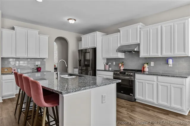 a kitchen with stainless steel appliances granite countertop a refrigerator a sink dishwasher a stove and white countertops with wooden floor