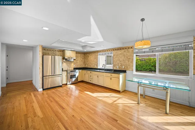 a kitchen with stainless steel appliances granite countertop a refrigerator a stove and a sink with wooden floors