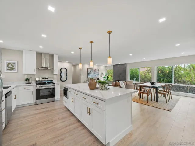a kitchen with stainless steel appliances kitchen island granite countertop a stove top oven a sink a dining table and chairs with wooden floor