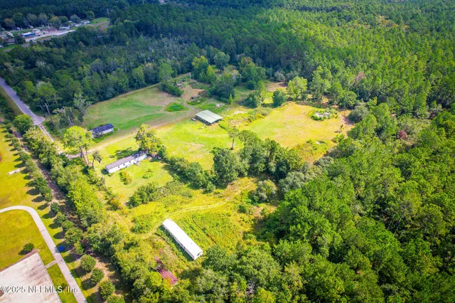 an aerial view of a residential houses with outdoor space and trees all around