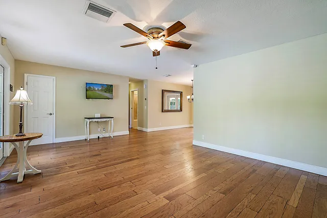 a view of an empty room with wooden floor and a ceiling fan