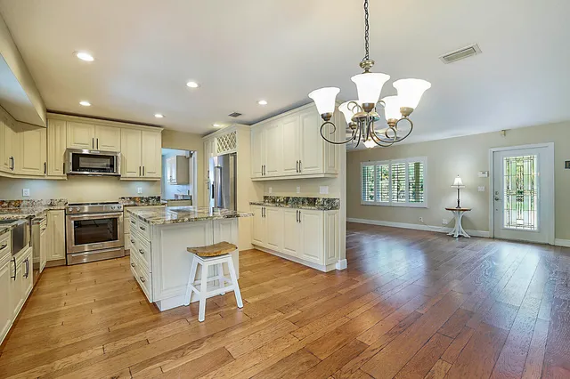 a kitchen with stainless steel appliances granite countertop a refrigerator a stove top oven a sink dishwasher a dining table and chairs with wooden floor