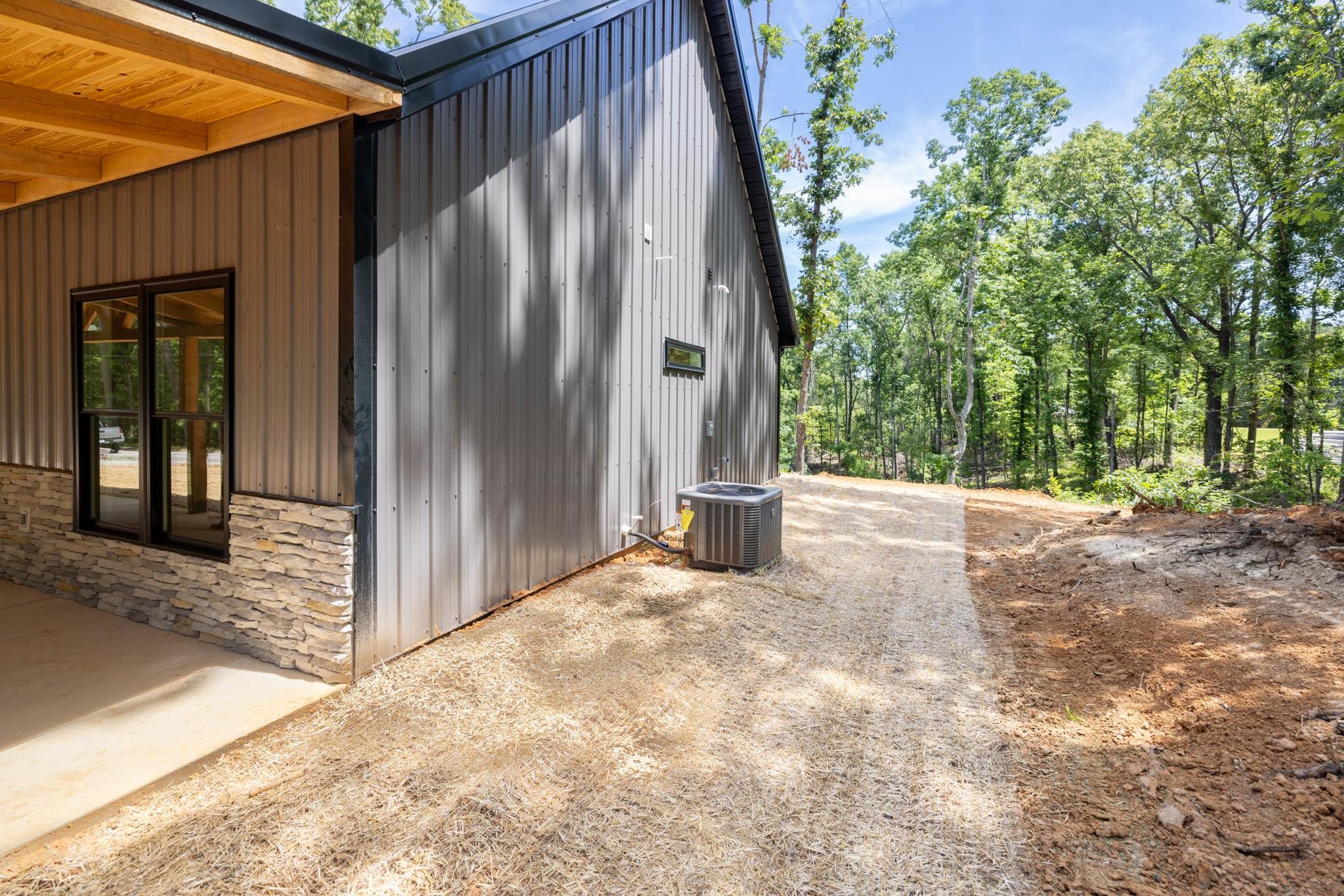 37 William Teague Lane Ramer, TN 38367 - Photo 5 of 39 Modern metal siding exterior with a stone veneer foundation, black-framed windows, and an exposed wood ceiling on the covered patio
