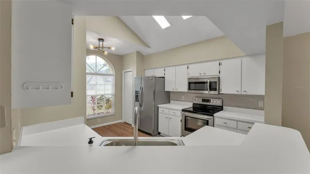 a kitchen with stainless steel appliances kitchen island granite countertop a refrigerator oven a sink dishwasher and white cabinets with wooden floor