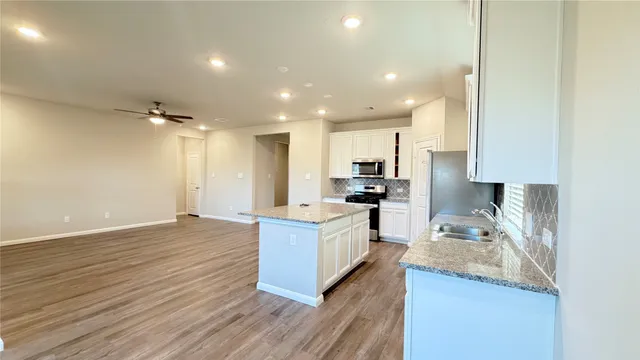 a large kitchen with kitchen island a stove a sink a refrigerator and white cabinets with wooden floor