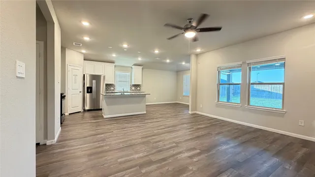a view of an empty room with wooden floor and a kitchen