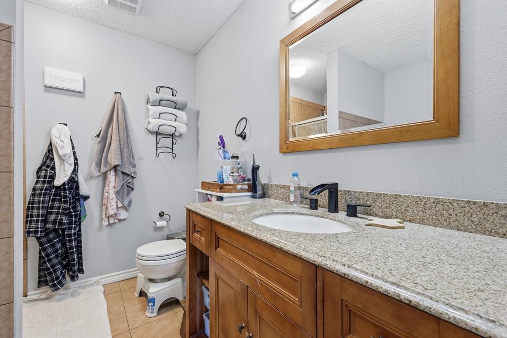 205 Comanche Trail Krum, TX 76249 - Photo 16 of 24 a bathroom with a granite countertop toilet sink and mirror
