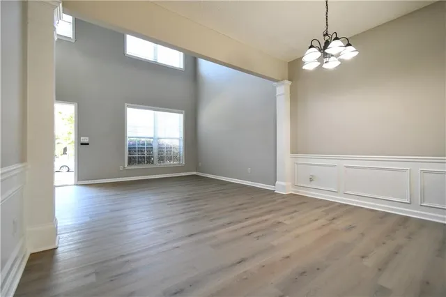 an empty room with wooden floor chandelier and windows