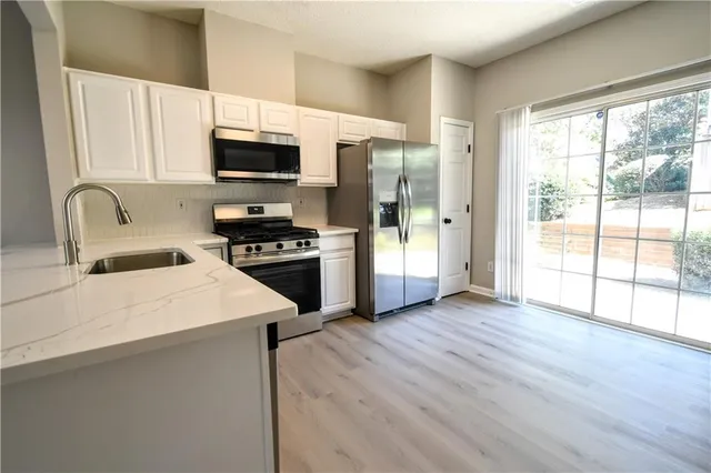 a kitchen with stainless steel appliances a microwave a stove a refrigerator white cabinets and wooden floor