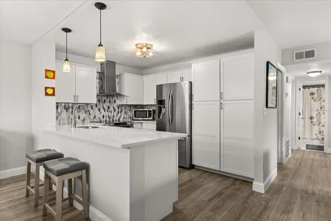 a kitchen with stainless steel appliances a refrigerator a sink dishwasher a stove and white cabinets with wooden floor