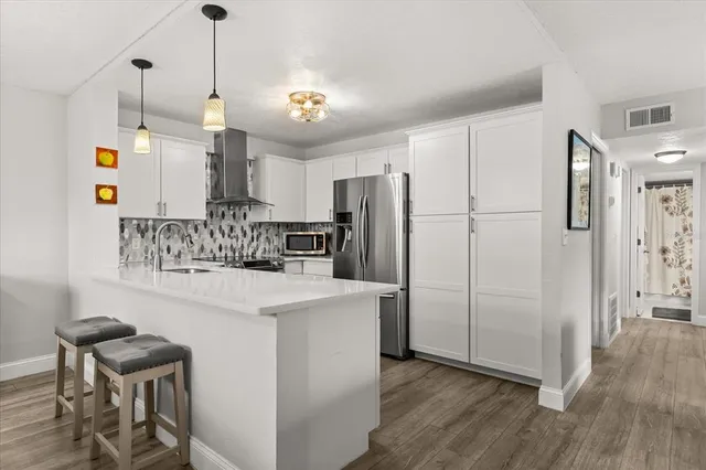 a kitchen with stainless steel appliances a refrigerator a sink dishwasher a stove and white cabinets with wooden floor