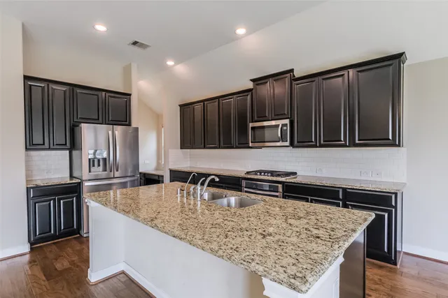 a kitchen with kitchen island granite countertop wooden cabinets a refrigerator and a sink