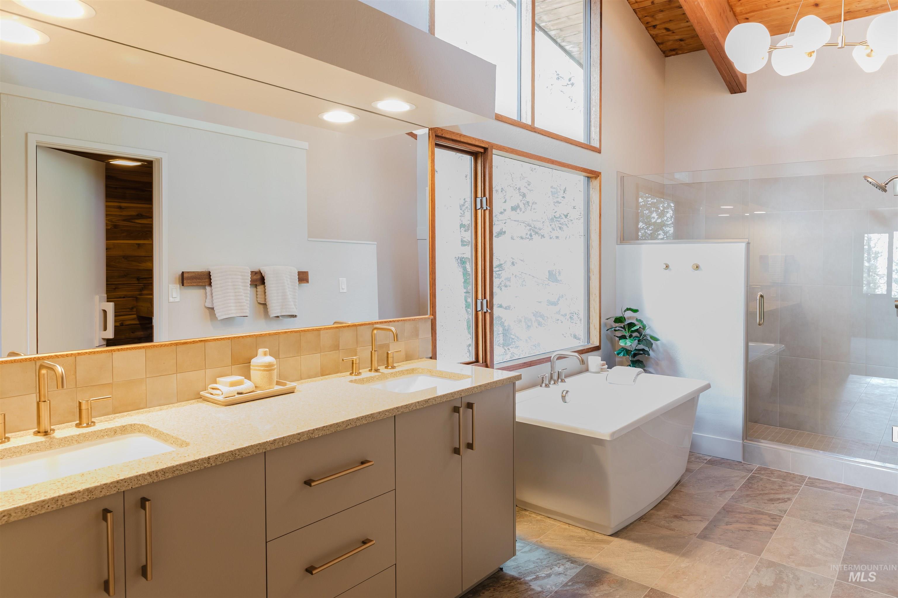 136 Silver Fox Trail McCall, ID 83638 - Photo 18 of 29 Dual vanity with integrated sinks and gold-finish fixtures, freestanding soaking tub, glass-enclosed shower, wood-finish vaulted ceiling, and large windows