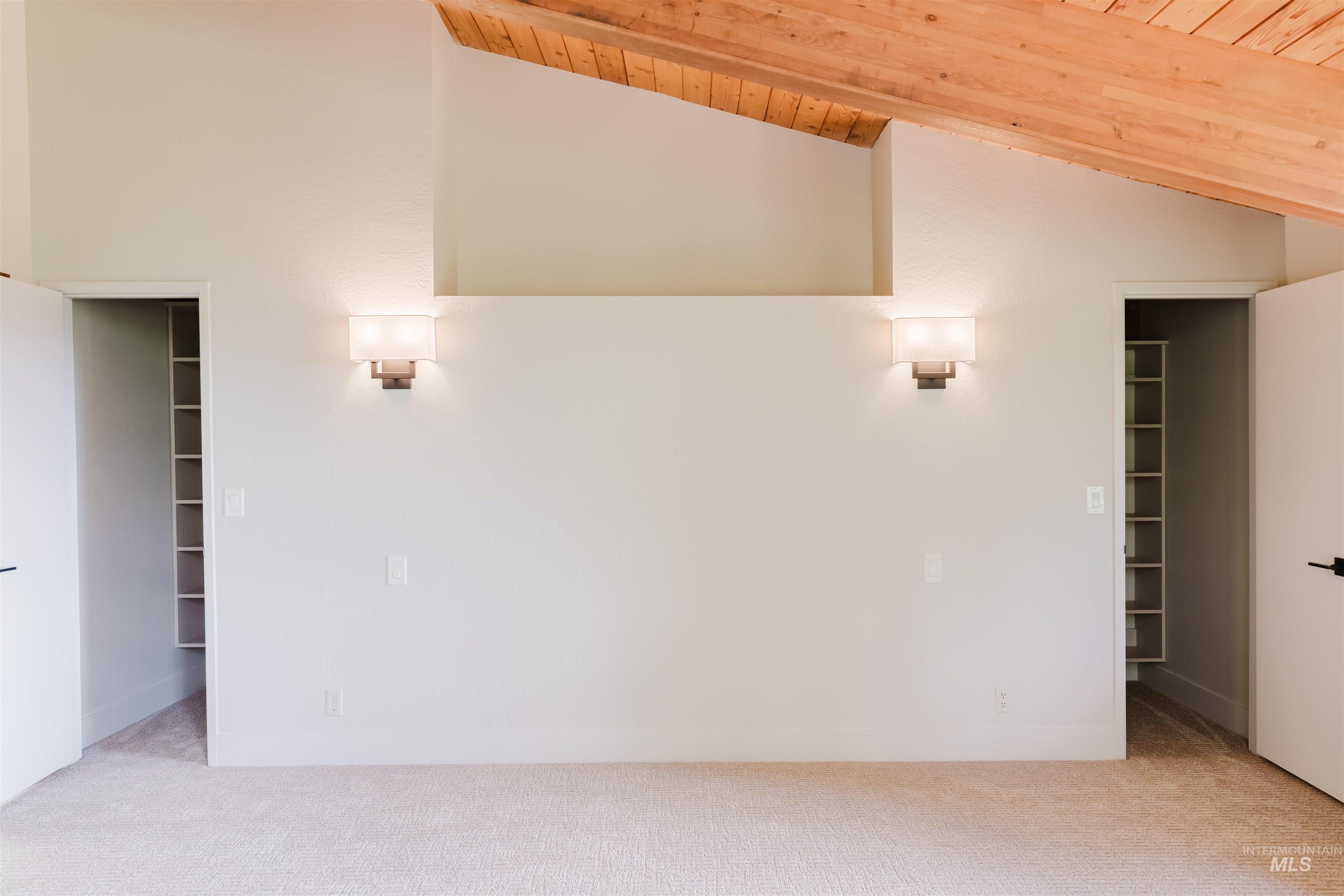 136 Silver Fox Trail McCall, ID 83638 - Photo 22 of 29 Vaulted ceiling with exposed wood beams, neutral wall paint, recessed shelving, wall-mounted sconces, and light-colored carpeting