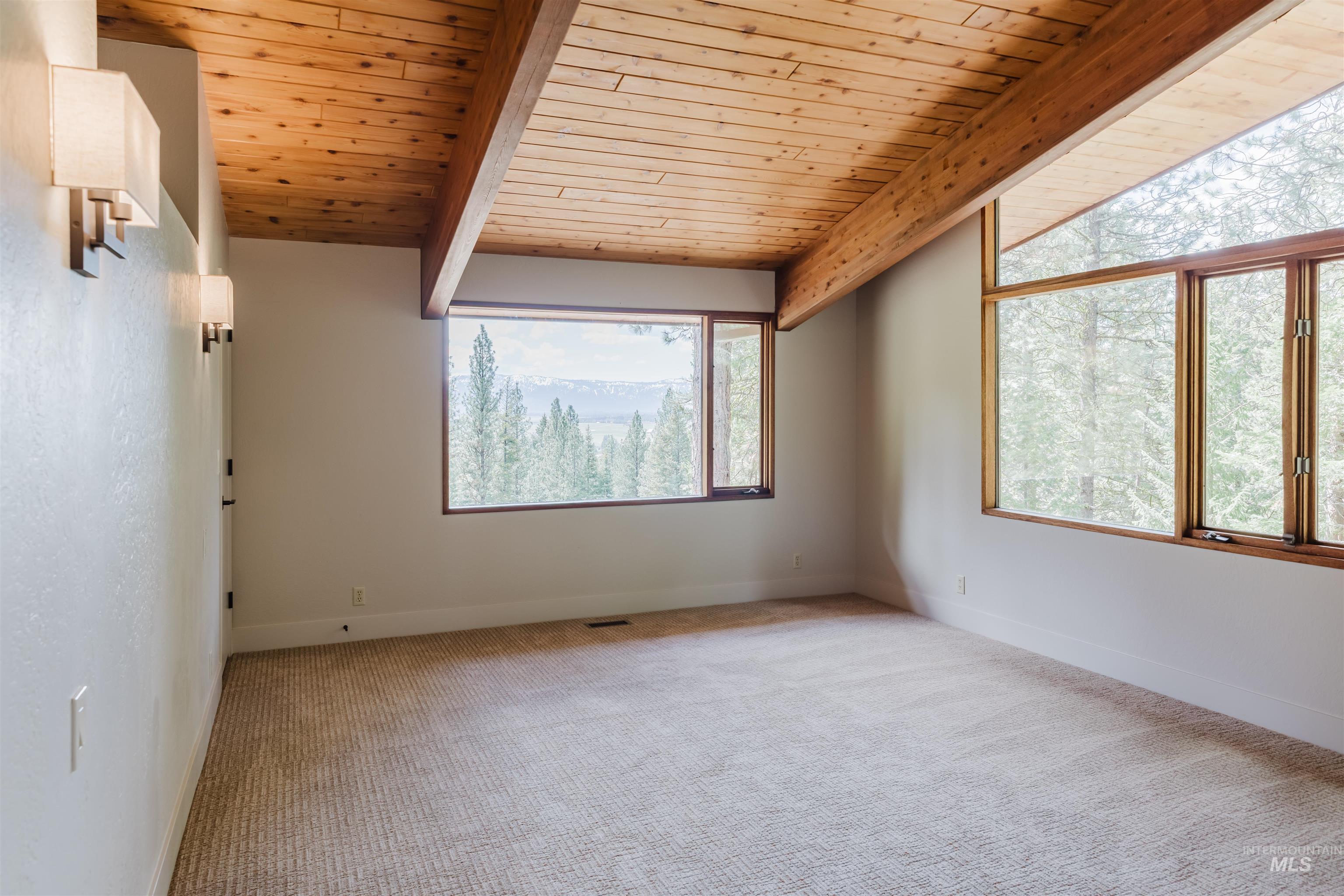 136 Silver Fox Trail McCall, ID 83638 - Photo 23 of 29 Vaulted wood-plank ceiling with exposed beams, expansive windows with wood framing, wall-mounted sconce lighting, and neutral tone carpeting